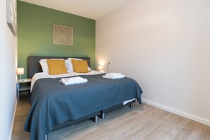 Un lit bien fait, recouvert d’une couvre-lit sombre, avec deux oreillers et un élément décoratif accroché au mur au-dessus.
