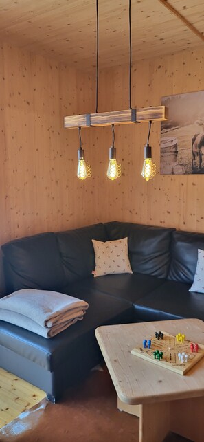 A cozy room with a black leather sofa, a wooden table with a board game, and three hanging light fixtures.