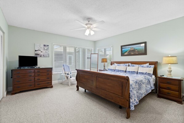 A bedroom with a wooden bed, a dresser, a TV, and a ceiling fan. - Tennis Tranquility-Cedars East #519 by RVA (Longboat Key)