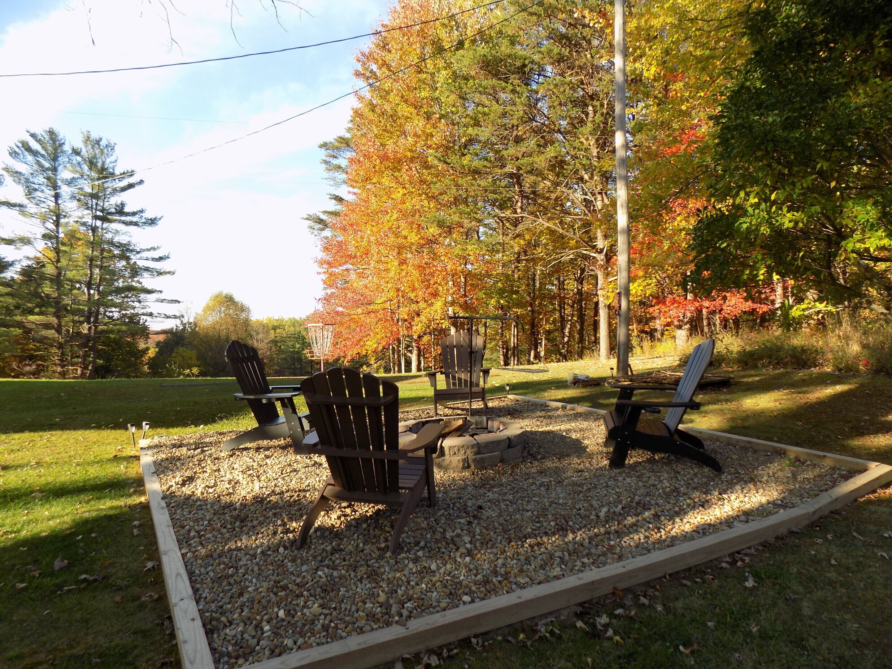 Un patio con sillas Adirondack, un hogar para fogata y una terraza de madera.