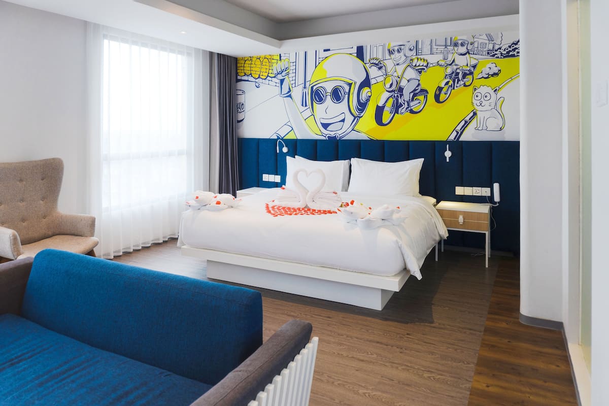 A modern hotel room with a large bed, a blue sofa, and a vibrant mural on the wall.