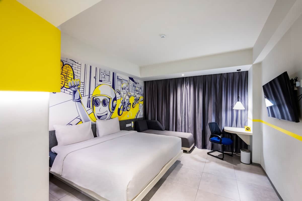 A modern hotel room with a large bed, a desk with a chair, a TV, and a mural on the wall.