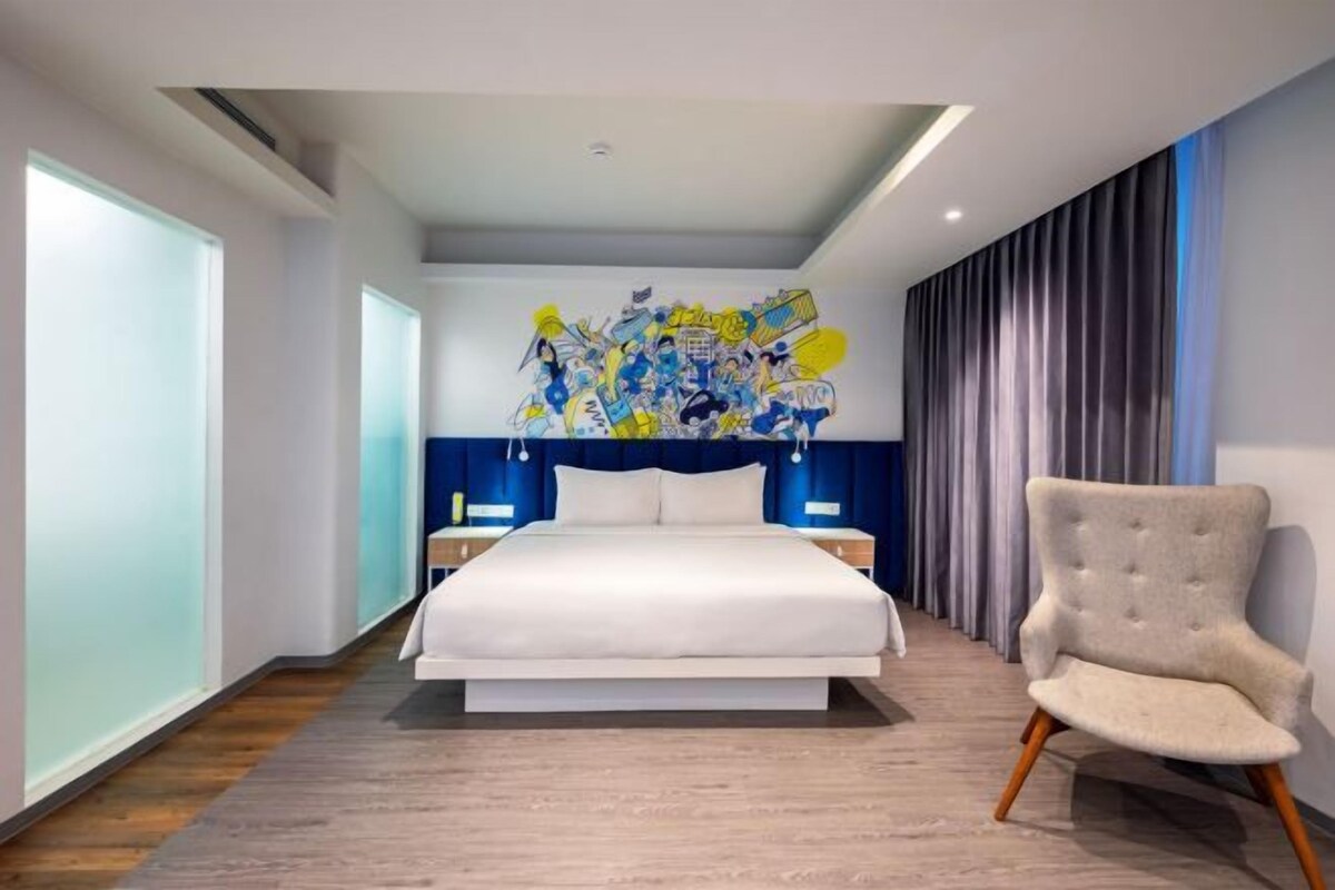 A modern hotel room with a large bed, a chair, and a unique wall mural.