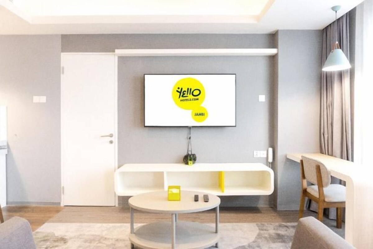 A modern hotel room with a flat-screen TV mounted on the wall, a white console table, a round coffee table, and a seating area with a chair.
