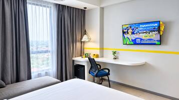 A hotel room with a bed, a desk, a chair, a television, and a window with curtains.
