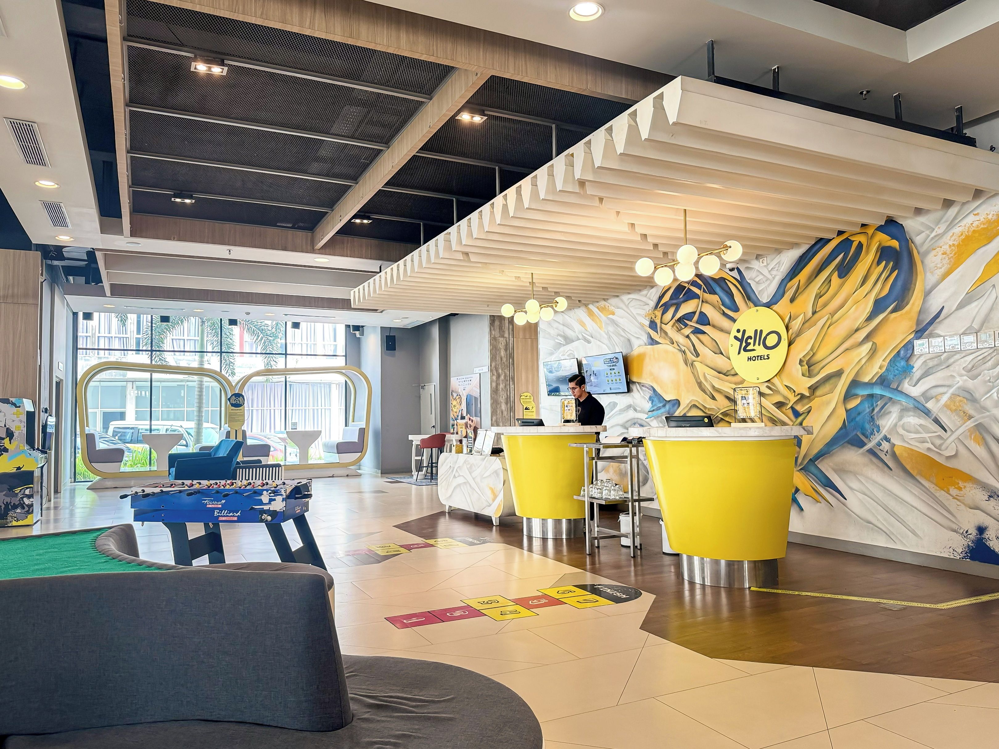 A hotel lobby with a reception desk, seating area, and a large mural.