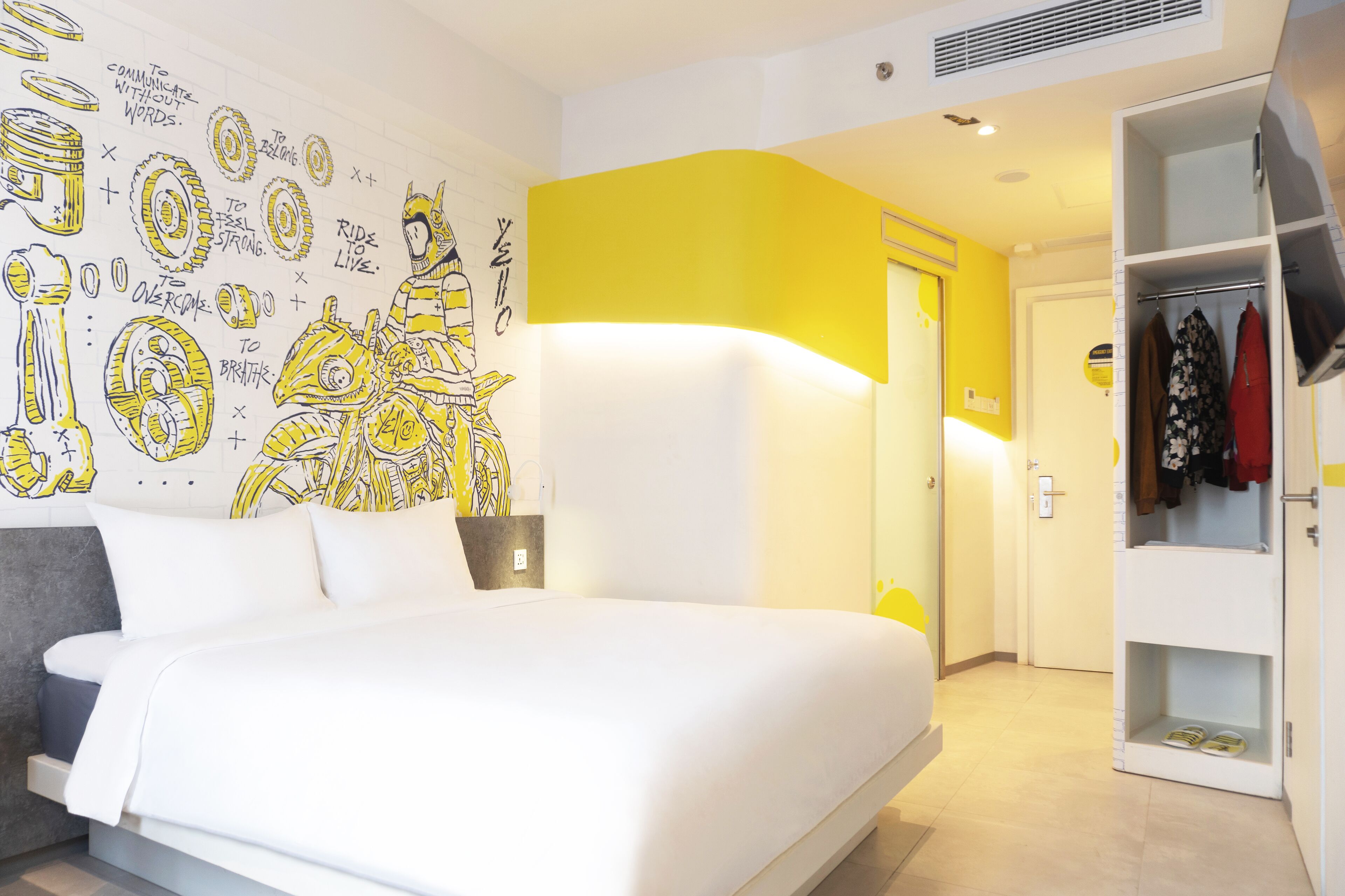 Una habitación de hotel moderna con una cama grande, un armario y una pared con ilustraciones motivacionales.