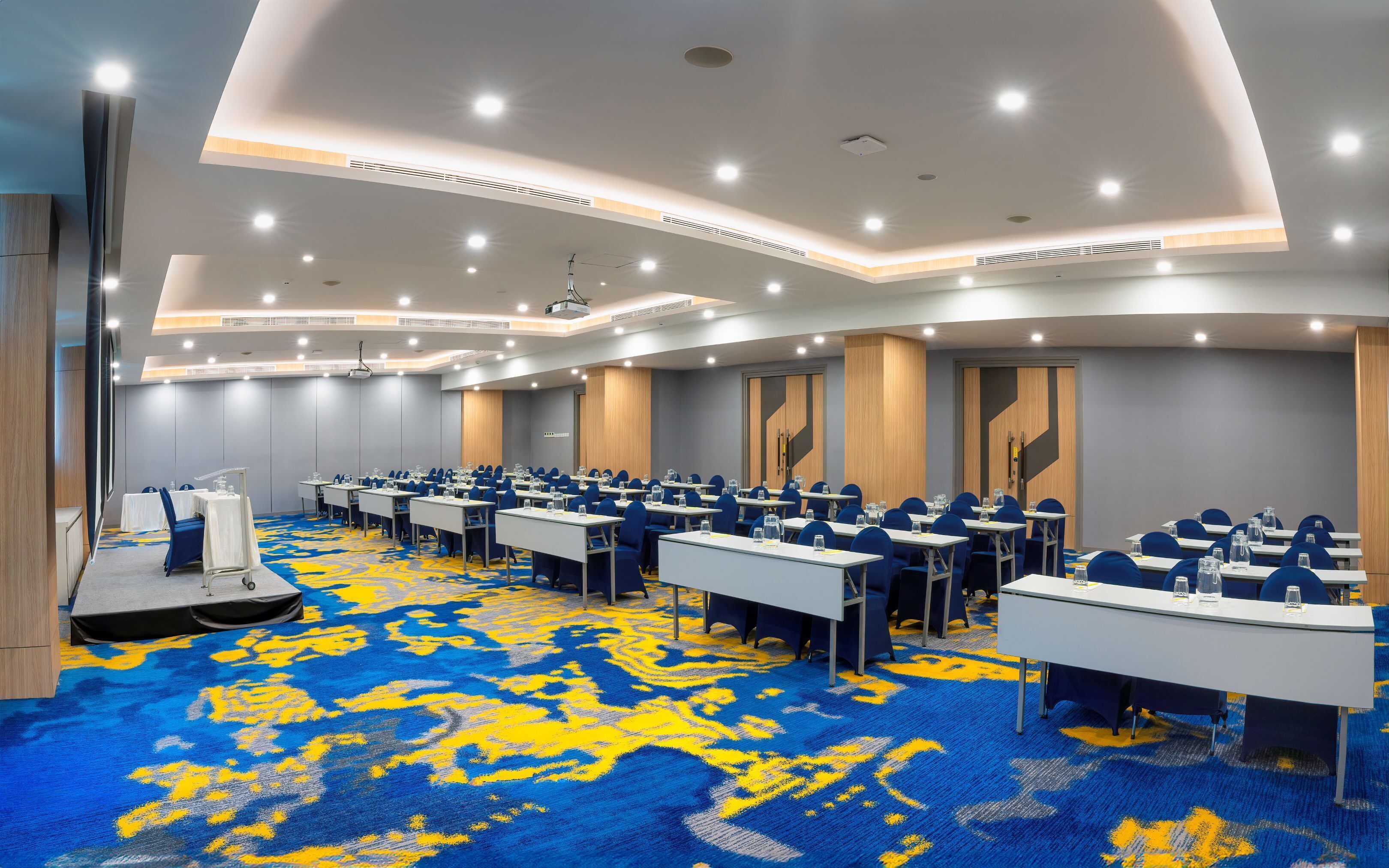 A conference room with multiple tables and chairs, a carpeted floor, and a modern ceiling design.