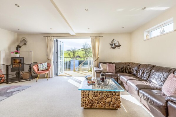 A living room with a sofa, a glass coffee table, a fireplace, and a view of the outdoors. - 4 Bed in Mortehoe (oc-dillyd) (Mortehoe)