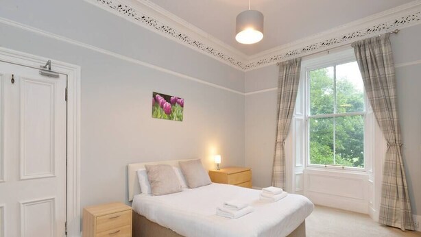 A bedroom with a bed, bedside tables, a window with curtains, and a door. - Home by The Meadows, close to City Centre (Edinburgh)