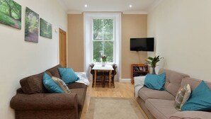 A living room with two sofas, a TV, a bookshelf, and a window with a view of greenery. - Home by The Meadows, close to City Centre (Edinburgh)