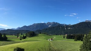 A rural landscape with a small white building, green fields, and a mountain range in the background. - Vacation apartment for 2 persons Hopferau (Hopferau)