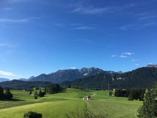 Paisaje rural con un pequeño edificio blanco, campos verdes y una cordillera en el fondo.
