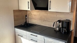 A compact kitchen with a black countertop, stainless steel appliances, and white cabinetry. - Vacation apartment for 2 persons Hopferau (Hopferau)