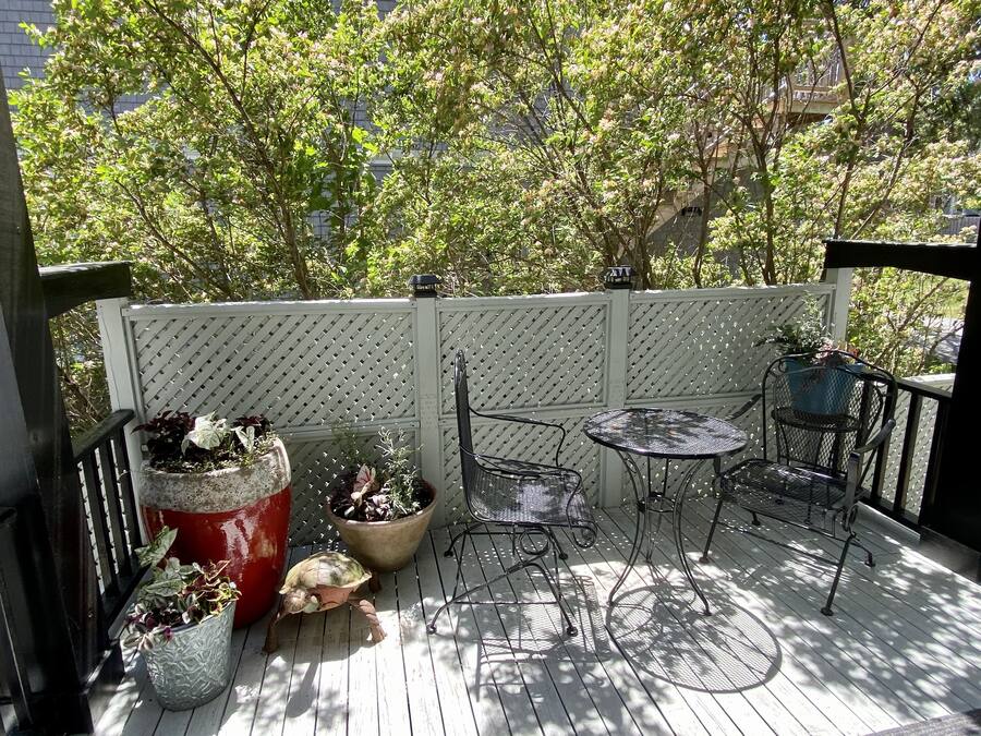 Una terraza de madera con cercado de celosía blanca, macetas, sillas y mesas de metal.