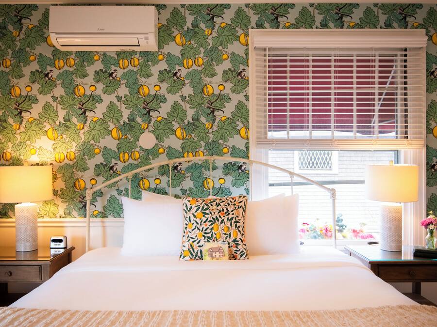 A neatly made bed with a white comforter and two pillows, a bedside lamp, and a nightstand with a lamp and a phone.