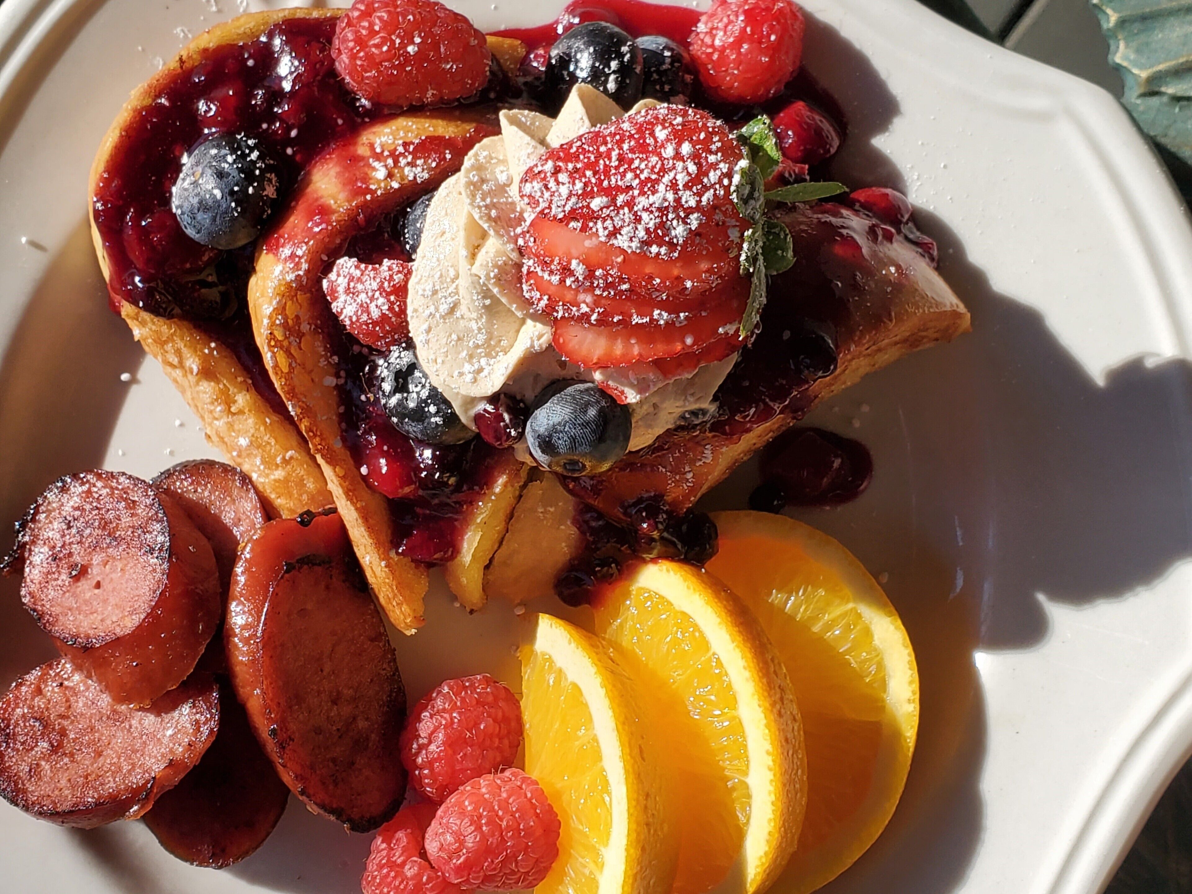 Un plato de gofres cubiertos de fresas, arándanos, frambuesas y rodajas de naranja.