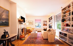 Una sala de estar acogedora con chimenea, un sofá, una mesita de centro y una estantería llena de libros y objetos decorativos.
