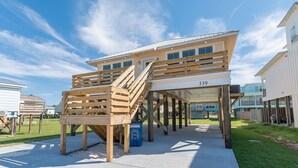 Une construction en bois à deux étages, dotée d’un escalier, portant le numéro 339, et comprenant un espace abrité avec une poubelle bleue.