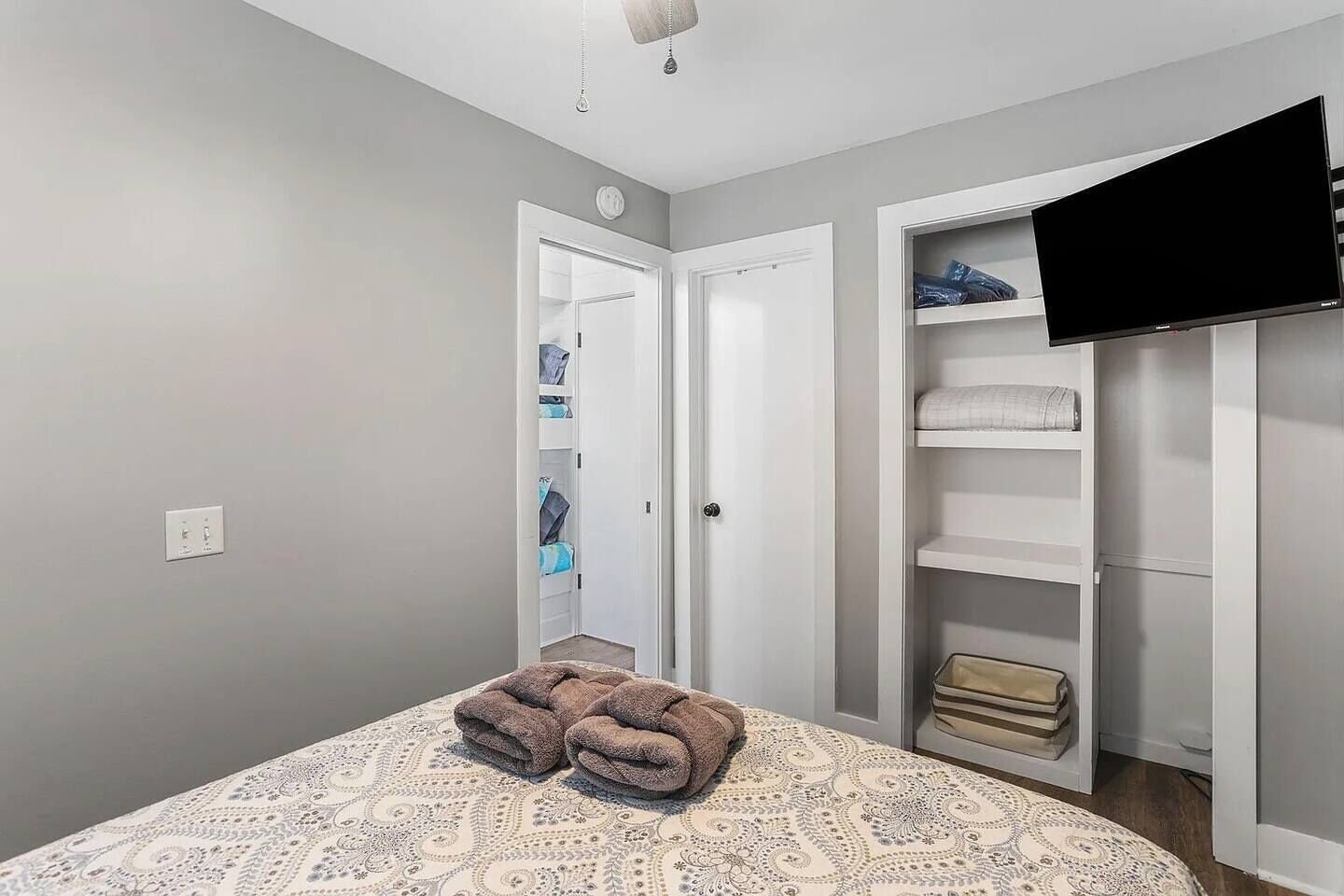 A bedroom with a bed, a closet with shelves, and a television.
