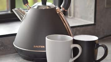 A modern kettle with a sleek design, a white mug, and a black mug on a kitchen counter near a window.