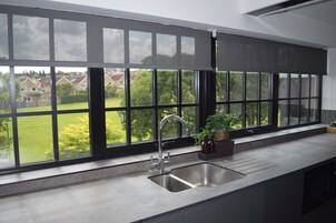 Una cocina con un amplio ventanal, un lavamanos de acero inoxidable y una planta en maceta en el alféizar.