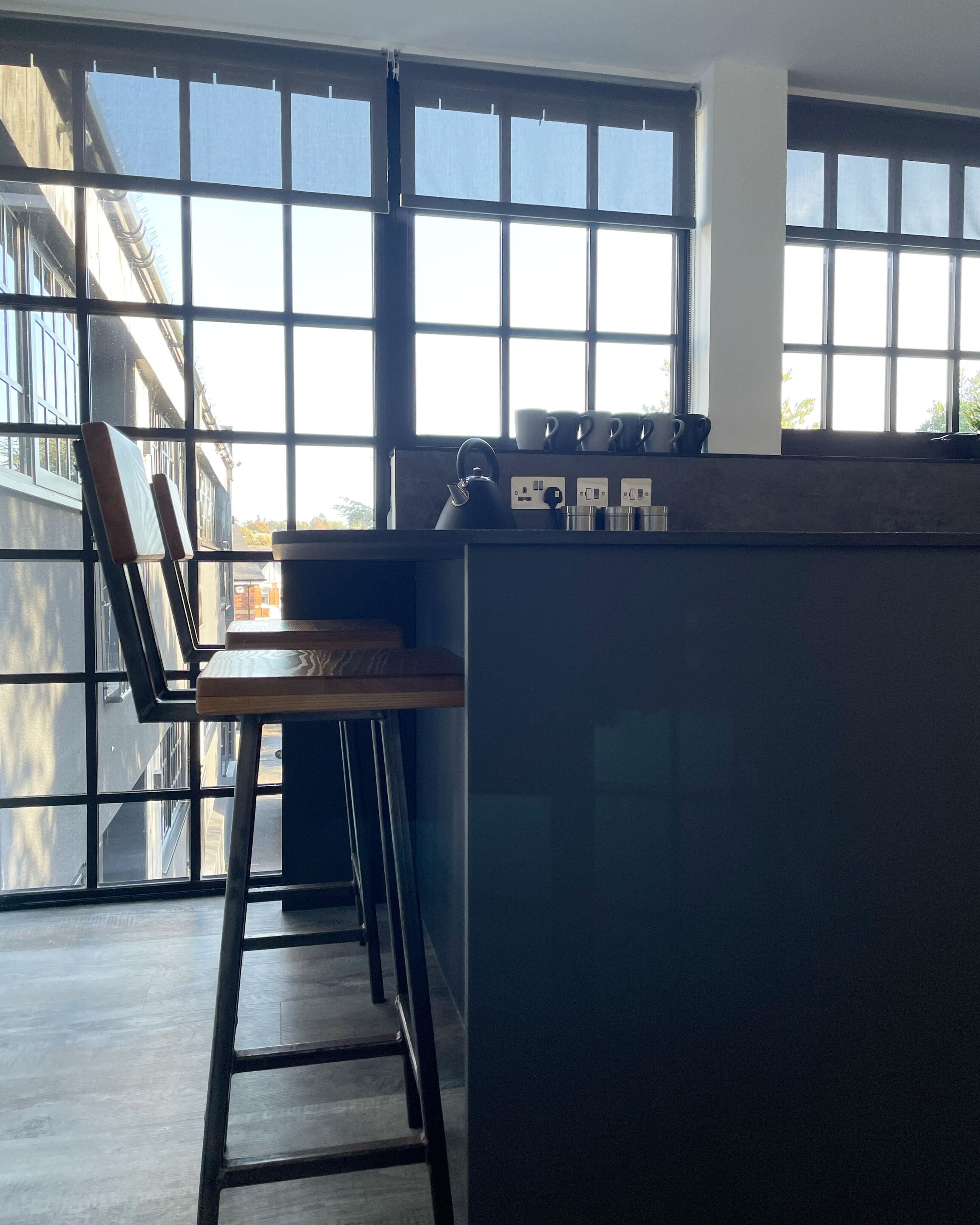 Una cocina moderna con ventanas amplias, una barra de madera y una tetera.