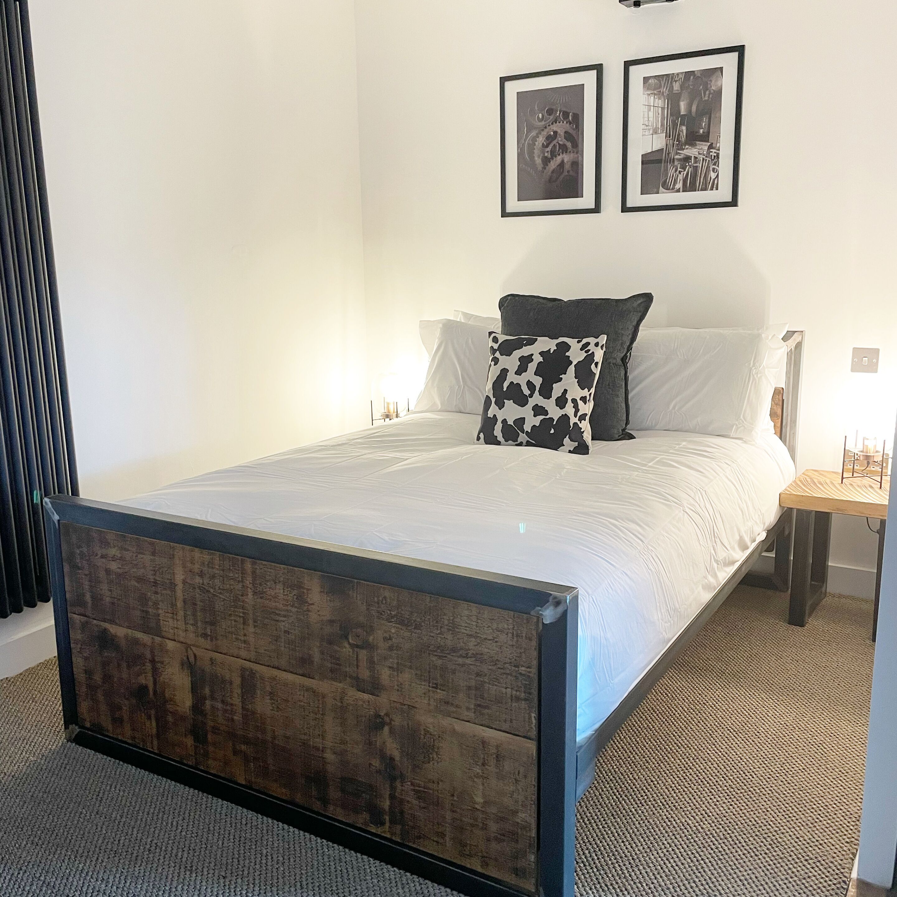 Ein Schlafzimmer mit einem Bettgestell aus Holz, weißer Bettwäsche, einem schwarz-weißen Kissen und zwei gerahmten Bildern an der Wand.