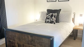 Ein Schlafzimmer mit einem Bettgestell aus Holz, weißer Bettwäsche, einem schwarz-weißen Kissen und zwei gerahmten Bildern an der Wand.