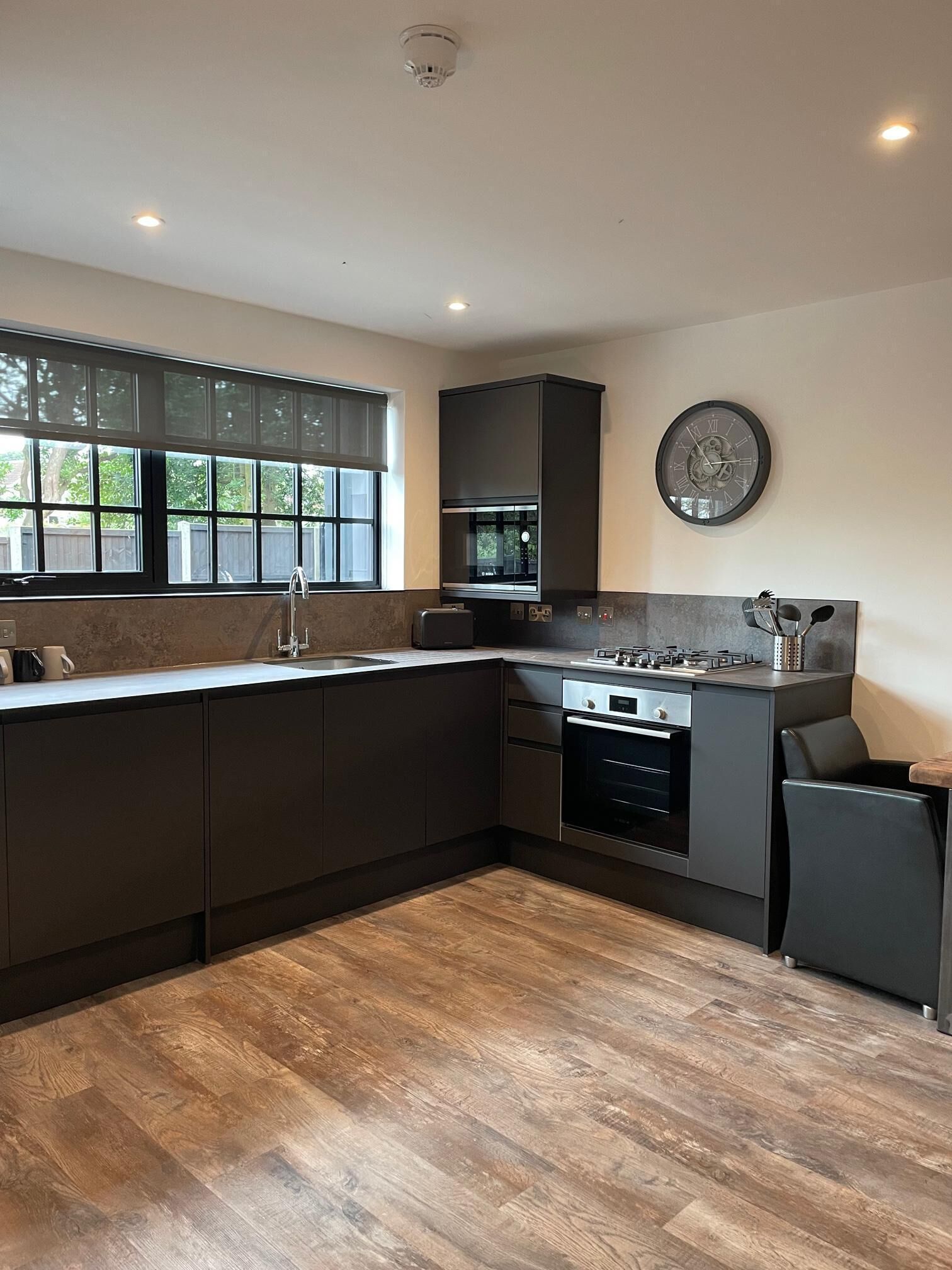 A modern kitchen with dark cabinetry, a large window, and a built-in oven.
