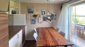 A modern kitchen with a wooden table, white chairs, and a large window with a view.