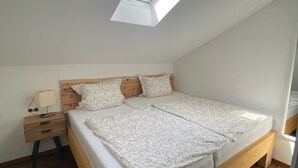 A bedroom with a skylight, wooden bed frame, white bedding, and a nightstand with a lamp.