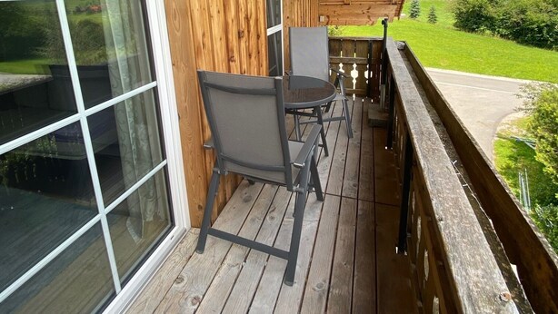 A wooden deck with a table and chairs, large windows, and a view of the countryside.