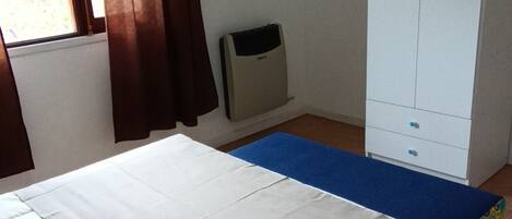 A bedroom with a bed, a wardrobe, a heater, and a window with curtains.