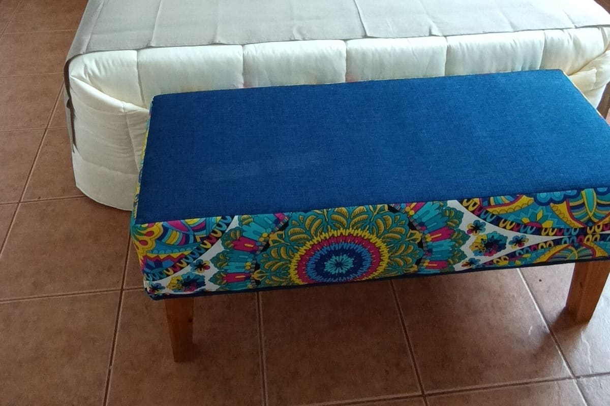 A bedroom with a large bed, two bedside tables, a colorful bench, and a tiled floor.