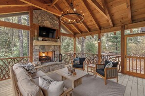 Une terrasse en bois avec une cheminée en pierre, des sièges confortables et une grande fenêtre donnant sur une forêt.