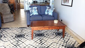 A living room with a blue sofa, patterned armchair, and a wooden coffee table. - Panoramic Ocean View Condo (Kihei)