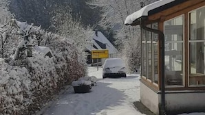 Ein verschneiter Weg führt zu einem Gebäude mit großen Fenstern und einer Holzanlage auf der rechten Seite.