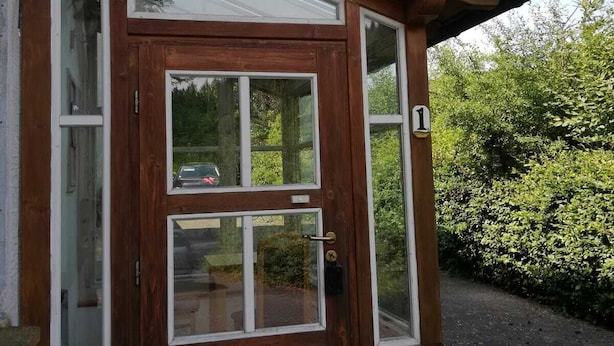 Eine Holztür mit Glasfenster, ein kleines Fenster darüber und die Zahl '1' auf der rechten Seite.