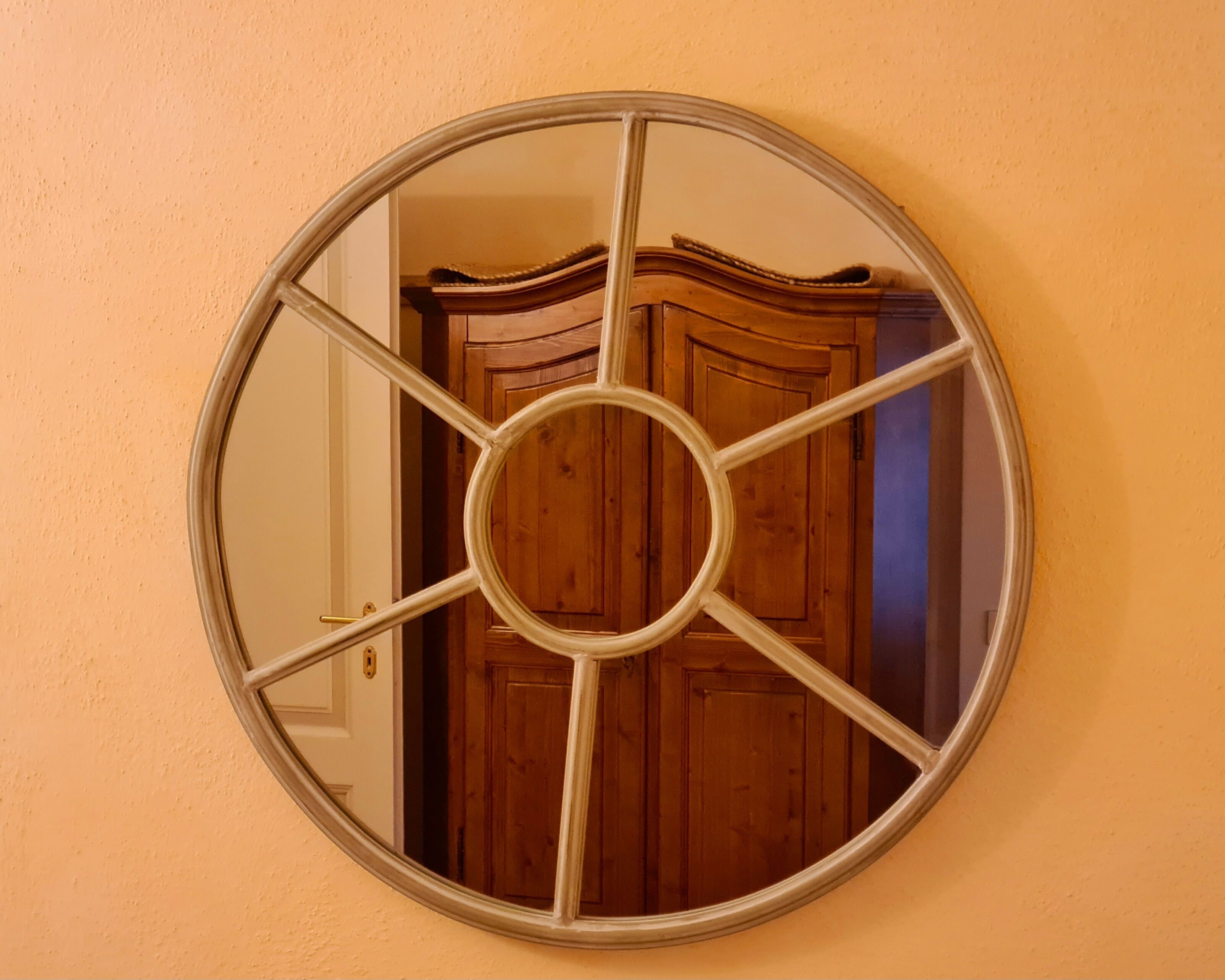 A round mirror with a central circular design, mounted on a peach-colored wall.