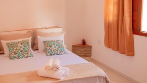 Ein Schlafzimmer mit einem Bett, Kissen, einem Nachttisch, einem Fenster mit Vorhängen und einer Wand-Klimaanlage.
