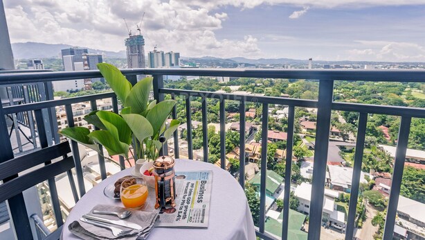 A balcony with a table set for breakfast, a newspaper, and a view of a cityscape with buildings and greenery. - Astonishing Home Office Balcony Cebu CBD Furnished (Cebu City)