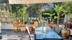 Une terrasse extérieure couverte, dotée d’une table à plateau de verre, de chaises et de plantes en pot.