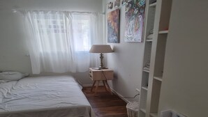 Une chambre à coucher avec un lit, une table de chevet avec une lampe, un panier en osier et une étagère blanche.