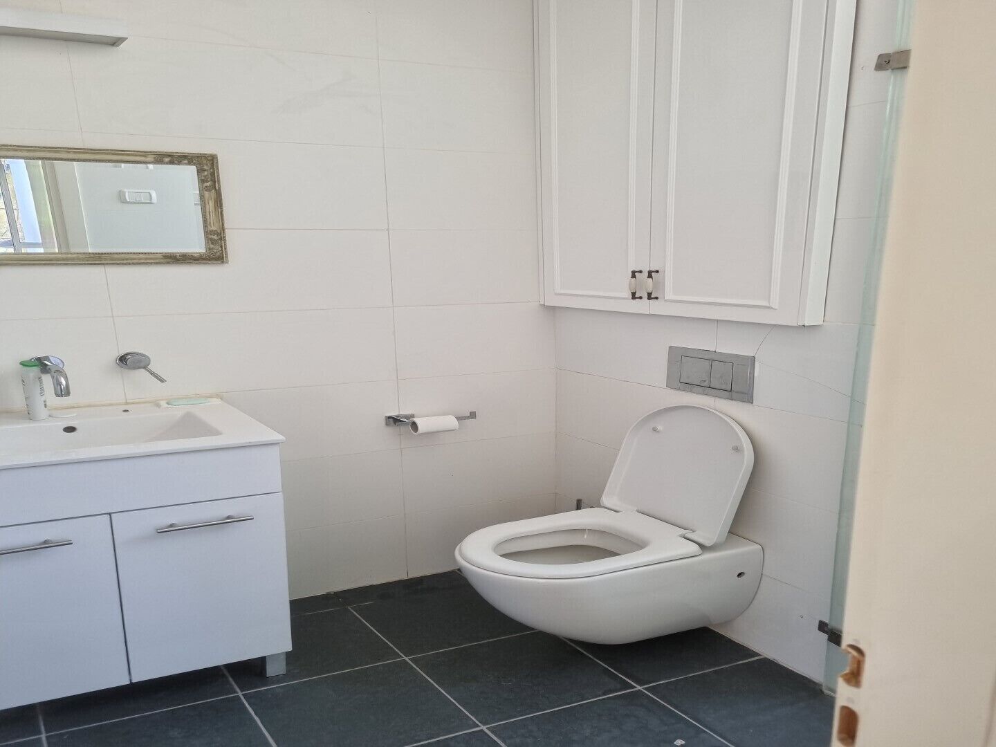 Une salle de bain avec un lavabo blanc, des toilettes et un miroir doté d’un cadre doré.