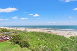 Une plage avec une promenade en bois, des parasols et une vue sur l’océan.