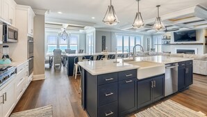 Une cuisine moderne dotée d’un grand îlot central, d’appareils électroménagers en acier inoxydable et offrant une vue sur l’océan.