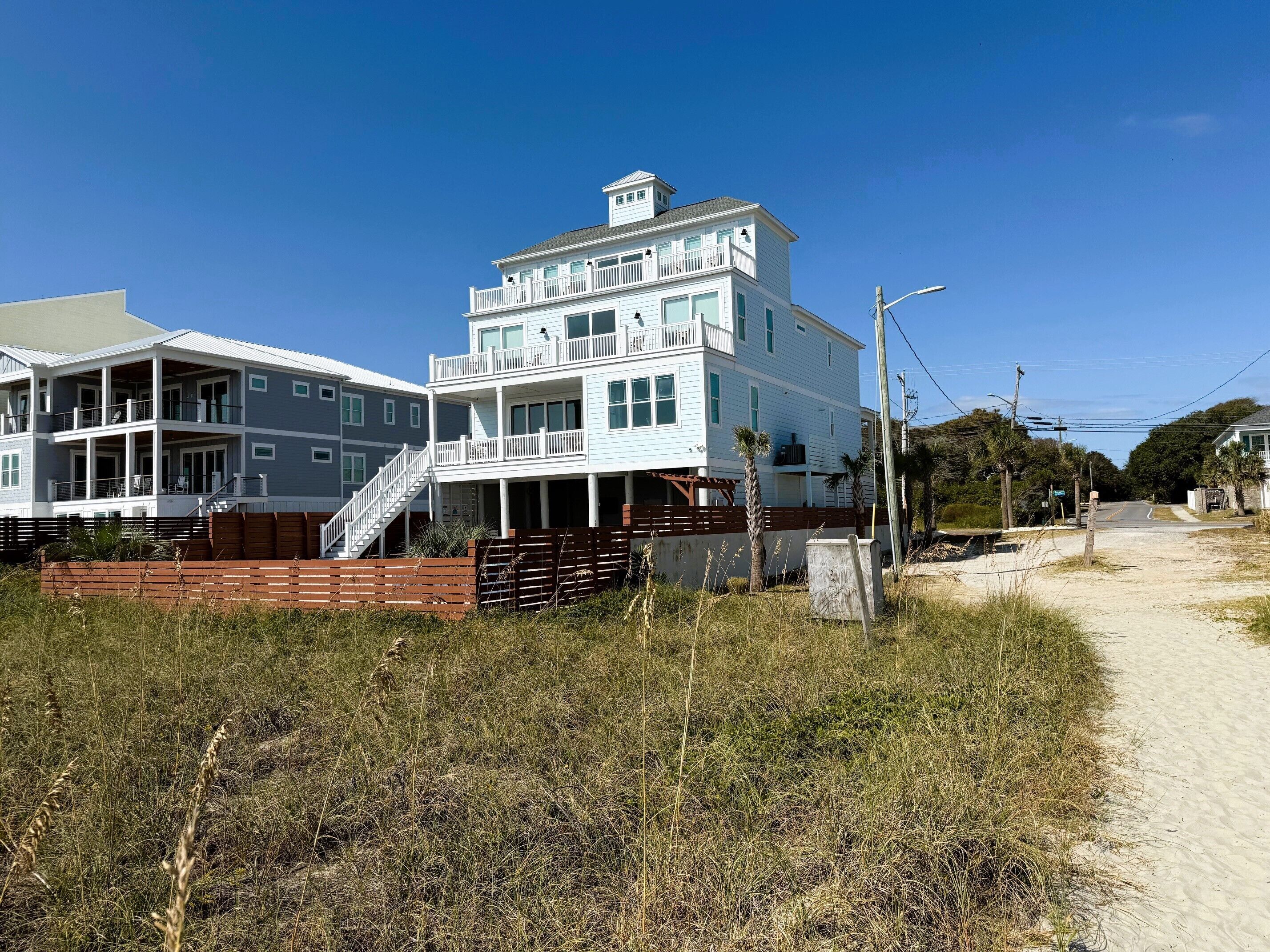 A multi-story beachfront house with a balcony, a covered porch, and a staircase leading to the upper levels.