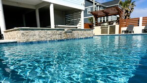 Une piscine aux eaux cristallines, bordée d’un mur en pierre et surmontée d’une pergola en bois.