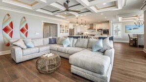 Un salon spacieux avec un canapé d’angle, un pouf rond et un ventilateur de plafond.